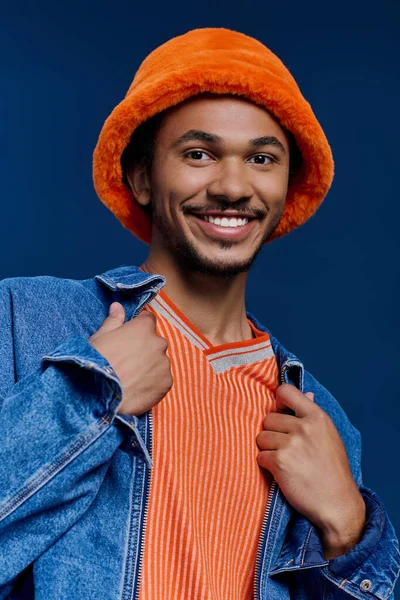 Şık bir genç adam neşeli bir şekilde ayakta duruyor, canlı kıyafetini ve hayat dolu kişiliğini gösteriyor..