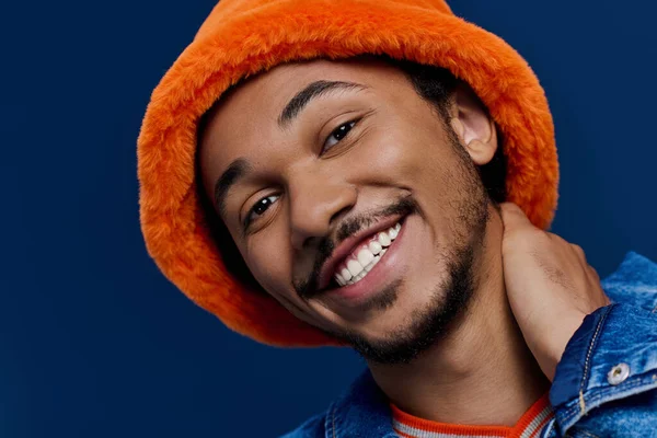 Neşeli genç bir adam çekici gülüşünü, parlak turuncu şapkasını ve günlük kıyafetlerini sergiliyor..