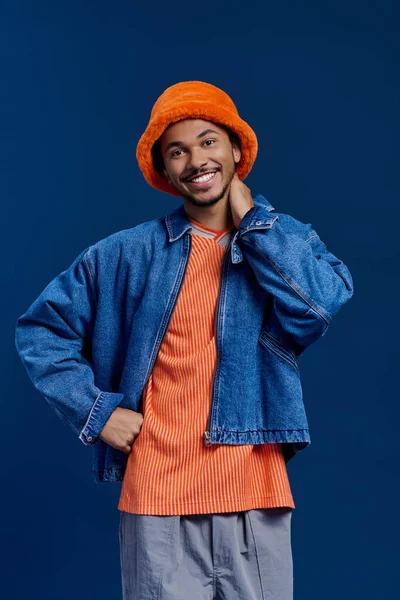 Neşeli bir ifadeyle genç yakışıklı bir adam parlak renklerle gösterişli bir kıyafet içinde poz veriyor..