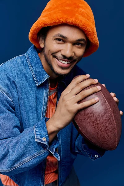 Şık bir genç adam elinde futbol topu tutarken, neşeli bir ruh sergileyerek ışıl ışıl gülümser..