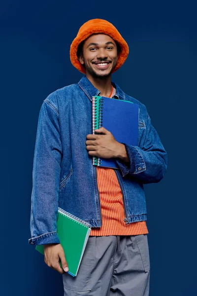 Şık turuncu şapkalı neşeli bir genç adam renkli defterleri canlı bir atmosferde tutar..