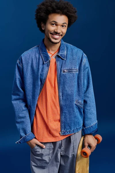 Parlak elbiseli genç adam bir kaykayla gülümsüyor, stüdyoda neşe saçıyor..