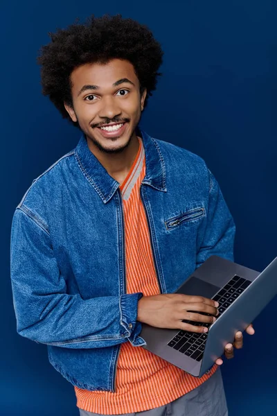 Kıvırcık saçlı neşeli genç bir adam dizüstü bilgisayarıyla meşgul, pozitif enerji yayıyor..