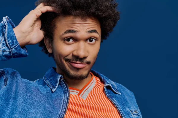 Genç, şık bir adam arsız bir gülümsemeyle kafasını parlak mavi bir arka fona sürtüyor..