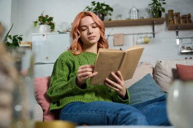 Konforlu bir oturma odasında, genç bir kadın huzur içinde büyüleyici bir kitaptan zevk alıyor..