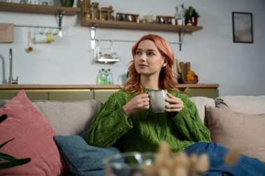 Dalgalı saçlarını kupadan yudumlayan, rahat evinin sıcaklığını kucaklayan hayat dolu genç bir kadın..