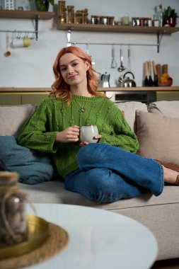 Güzel, genç bir kadın, rahat bir içki yudumlarken şık bir oturma odasında dinleniyor..