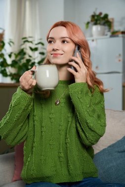 Gülümseyen kadın telefonda konuşurken elinde bir fincan kahve tutuyor. Parlak, davetkar bir yerde..