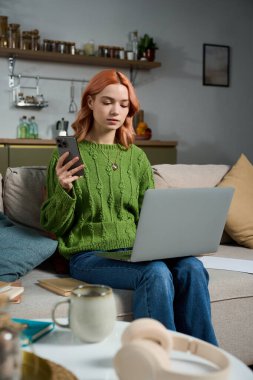 Rahat bir odada, yeşil kazaklı genç bir kadın iş yerinde birden fazla iş yapıyor..