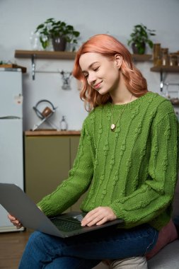 Young woman with pink hair enjoys working on her laptop in a vibrant, welcoming space.