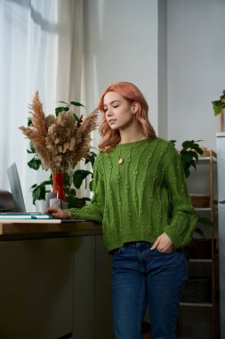 Güzel genç bir kadın rahat yeşil bir süveter içinde duruyor, etrafı doğa ile çevrili..