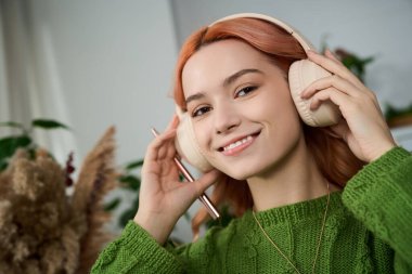 Güzel saçlı genç bir kadın, rahat bir atmosferde büyük kulaklıklar takarak müzik dinlemekten zevk alır..