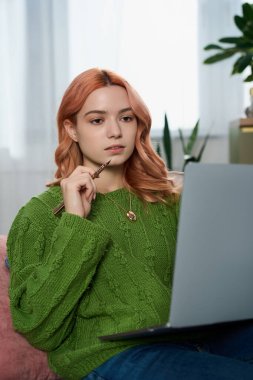 Samimi yeşil kazaklı genç bir kadın dikkatle dizüstü bilgisayarına odaklanıyor..