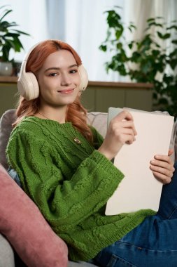 Kulaklıklı genç ve güzel bir kadın kanepede dinleniyor, rahat bir oturma odasında resim çiziyor..