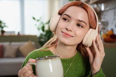 Kulaklıklı mutlu genç bir kadın sıcak ve davetkar bir atmosferle çevrili çayı yudumluyor..