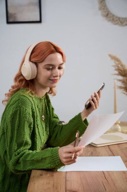 Parlak ışıklı odada yeşil kazaklı genç bir kadın var. Telefonunu kullanırken gülümsüyor..