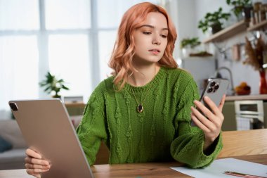 Dalgalı saçlı güzel genç bir kadın akıllı telefonuna bakıyor, evde düşüncelere dalmış..