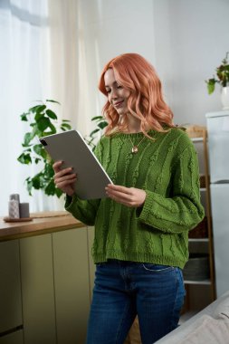 In a peaceful room filled with plants, a cheerful young woman engages with her tablet, smiling.
