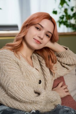 Işıl ışıl aydınlatılmış odada pembe saçlı, somut rahatlığı ve zarafeti olan hoş bir genç kadın var..