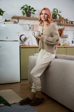 Güzel genç bir kadın modern yaşam alanında rahatlar, kahvesini yudumlar ve rahatına bakar..