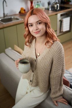 Genç bir kadın sıcak içeceğinin tadını çıkarıyor, büyüleyici bir mutfak alanında mutluluk saçıyor..