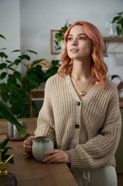 Yumuşak pembe saçlı güzel genç bir kadın ahşap tezgahın yanında duruyor, sıcak bir içkinin tadını çıkarıyor..