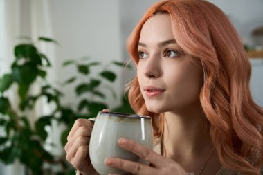 Pembe saçlı genç bir kadın elinde buharlı bir kupa tutuyordu. Düşüncelere dalmış, yeşil alanda kaybolmuştu..