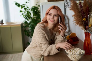 Güzel genç bir kadın mutfağında, elinde kaşıkla gevşiyor, taze atıştırmalıklarla çevrili..