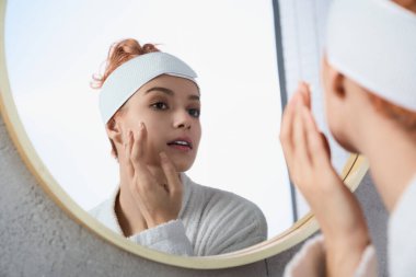 Genç bir kadın, yuvarlak bir aynaya bakıp kendine bakmak için biraz zaman ayırır..