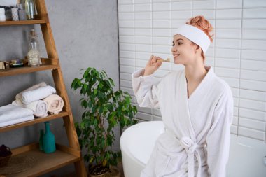 Işıl ışıl genç bir kadın sakin bir banyoda kendine bakmaktan zevk alıyor, mutluluk saçıyor..