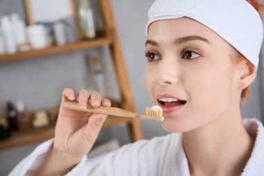 Genç bir kadın, sıcacık bir banyoda dişlerini fırçalıyor. Mutlulukla sıhhatini kucaklıyor..