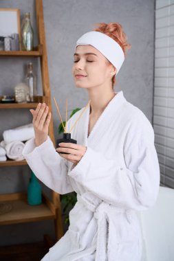 Beyaz cüppeli genç bir kadın spa 'da huzurlu bir anın tadını çıkarırken rahatlatıcı kokuları kucaklıyor..