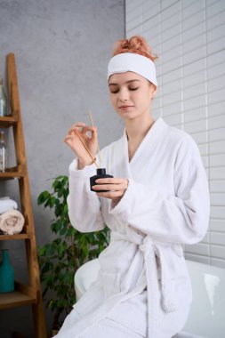 Rahat bir bornoz giymiş genç ve güzel bir kadın sakin bir banyoda otururken aroma terapisine başlıyor..