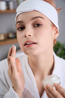 Genç bir kadın, sakin bir kaplıcada dinlenirken yüzüne krem sürüyor..