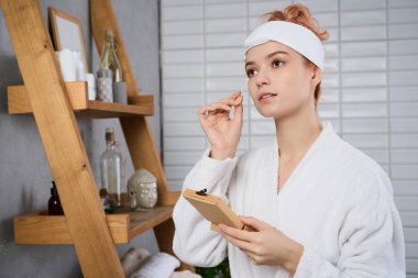 Genç bir kadın cilt bakımı ritüelinden zevk alır. Odaklanmış ve huzurlu bir şekilde güzel bir banyoda..