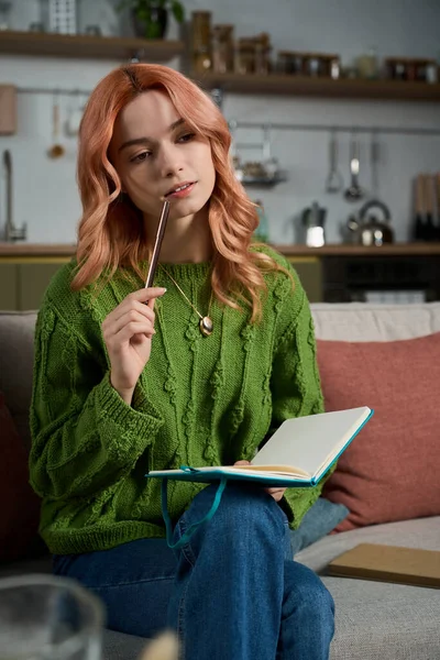 Genç bir kadın rahat bir oturma odasında dinleniyor, düşünceli bir şekilde günlüğünü yazıyor..