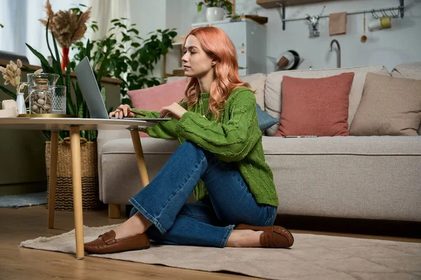 Genç bir kadın dizüstü bilgisayarı ile şık bir dekorun arasında yerde oturuyor..