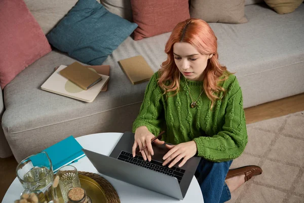 Dizüstü bilgisayarına odaklanmış, rahat bir oturma odasında oturan güzel bir genç kadın..