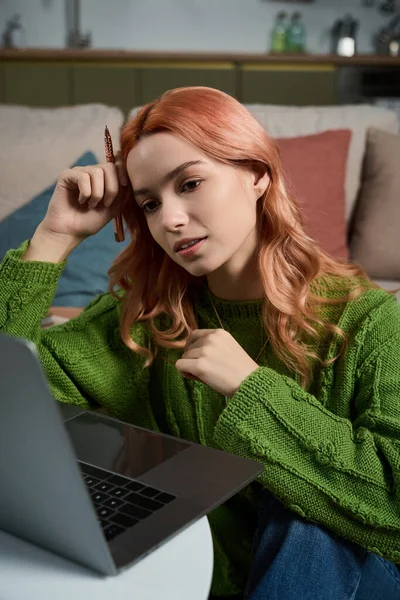 Pembe saçlı genç bir kadın laptopuna odaklanmış, rahat bir ortamda düşüncelere dalmış..