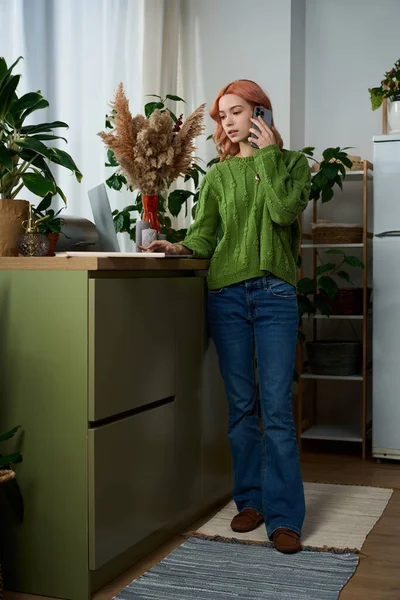 Yeşil kazaklı bir kadın mutfak tezgahının yanında telefonla konuşuyor..