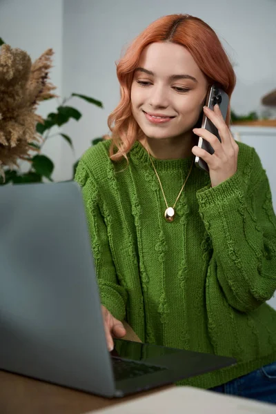 Güzel genç bir kadın bilgisayarında yazarken telefonuyla konuşuyor. Etrafı bitkilerle çevrili..