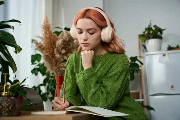 Yeşil kazaklı genç bir kadın, iç mekan dolu, huzurlu bir bitkiye yazar..