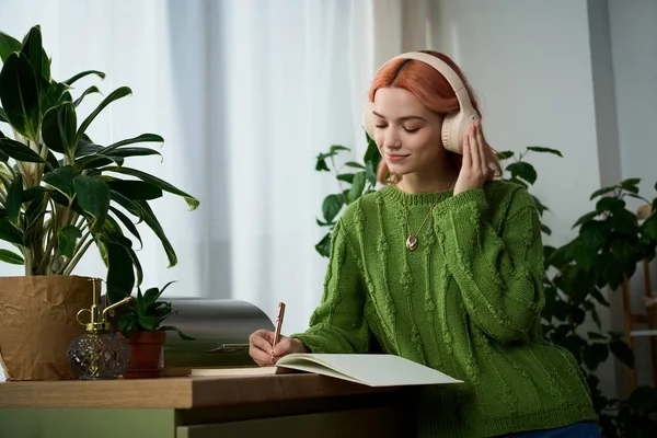 Kulaklıklı genç bir kadın defterine, yemyeşil bitkilerin ve sıcak güneş ışığının arasında yazıyor..