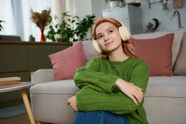 Güzel genç bir kadın canlı yeşil bir kazakla rahatça otururken müzik dinler..