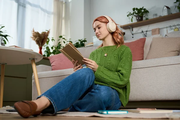 Güzel genç bir kadın modern evinde bir kitap ve müzikle huzurlu bir anın tadını çıkarıyor..