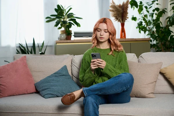 Pembe saçlı genç bir kadın rahat bir şekilde koltukta oturuyor, telefonuna dalmış, dinleniyor..