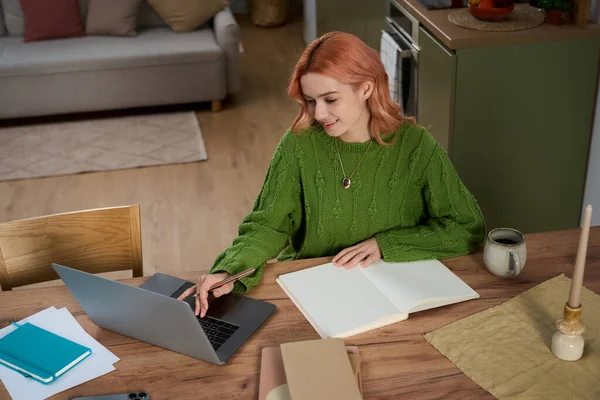 Pembe saçlı güzel bir kadın laptopunu sıcak bir ortamda kullanırken notlar yazıyor..