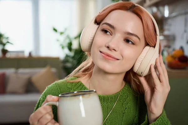 Kulaklıklı mutlu genç bir kadın sıcak ve davetkar bir atmosferle çevrili çayı yudumluyor..