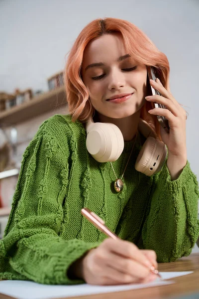 Güzel, genç bir kadın, fikirlerini şık bir masada yazarken telefonla konuşmaktan zevk alır..