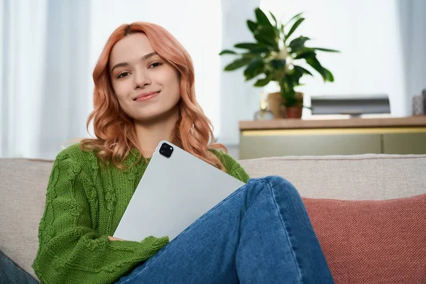 Parlak ve neşeli genç bir kadın, elinde bir tabletle kanepede gevşer, hayat dolu bir dekorla..